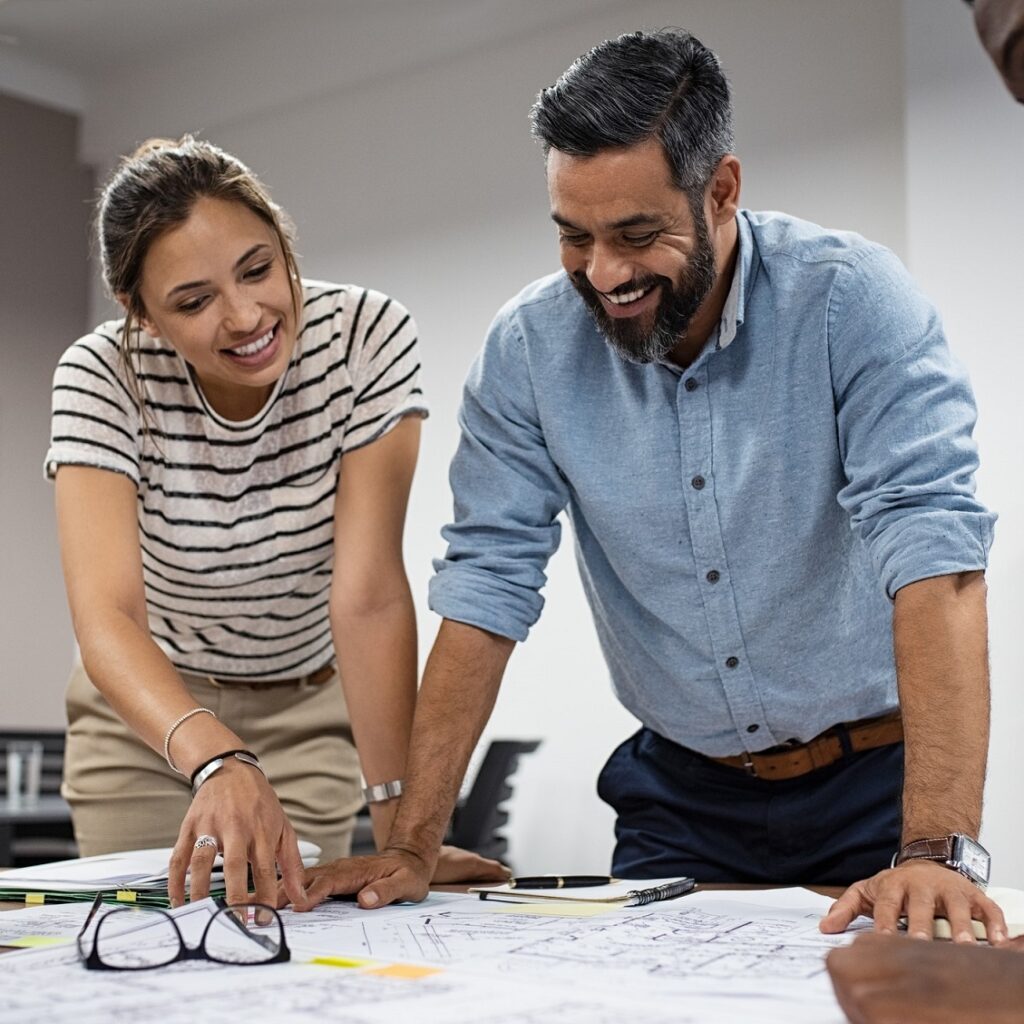 Eine Frau und ein Mann diskutieren lächelnd und zeigen dabei auf ein Gebäudeplan.