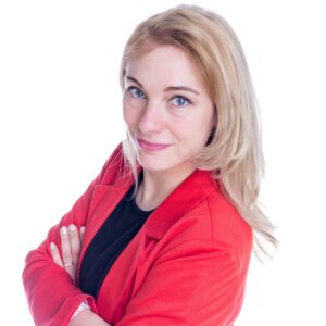 Eine blonde Frau im roten Blazer, Prof. Dr. Sandra Niedermeier, schaut mit verschränkten Armen seitlich über die Schulter lächelnd direkt in die Kamera.