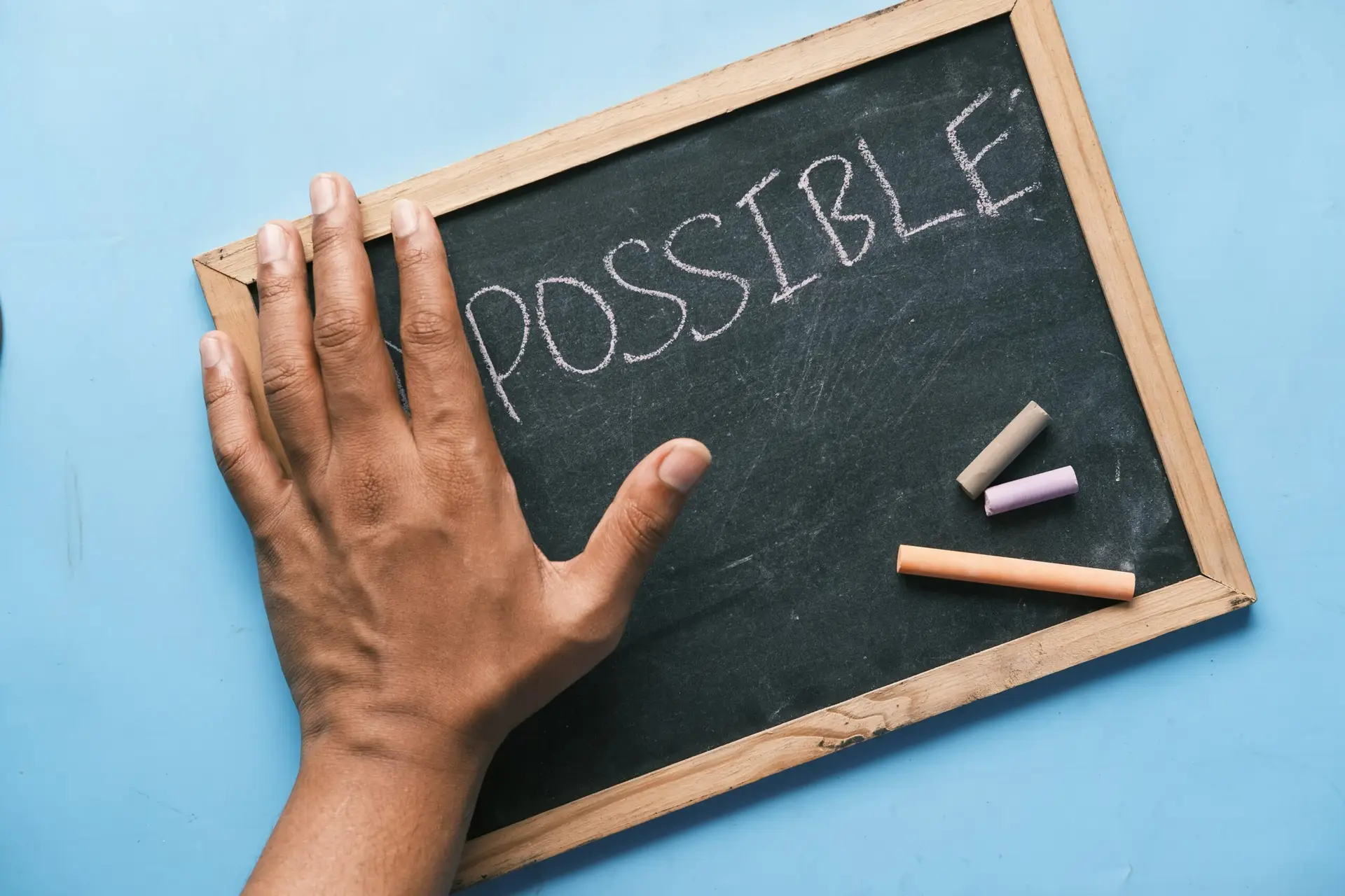 Ein dekoratives Header-Bild für Leading Change Haltung statt Methode, eine Schiefertafel auf der Possible steht, eine Hand verdeckt einen Teil, es suggeriert, ein "im"- also würde eigentlich Impossible stehen.