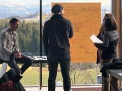 Gruppe von Personen stehen vor einem Flipchart.