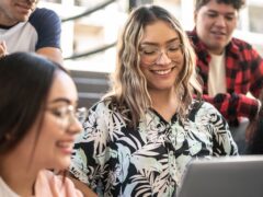 Blonde Frau schaut auf ihren Laptop, umgeben von 3 weiteren Personen.