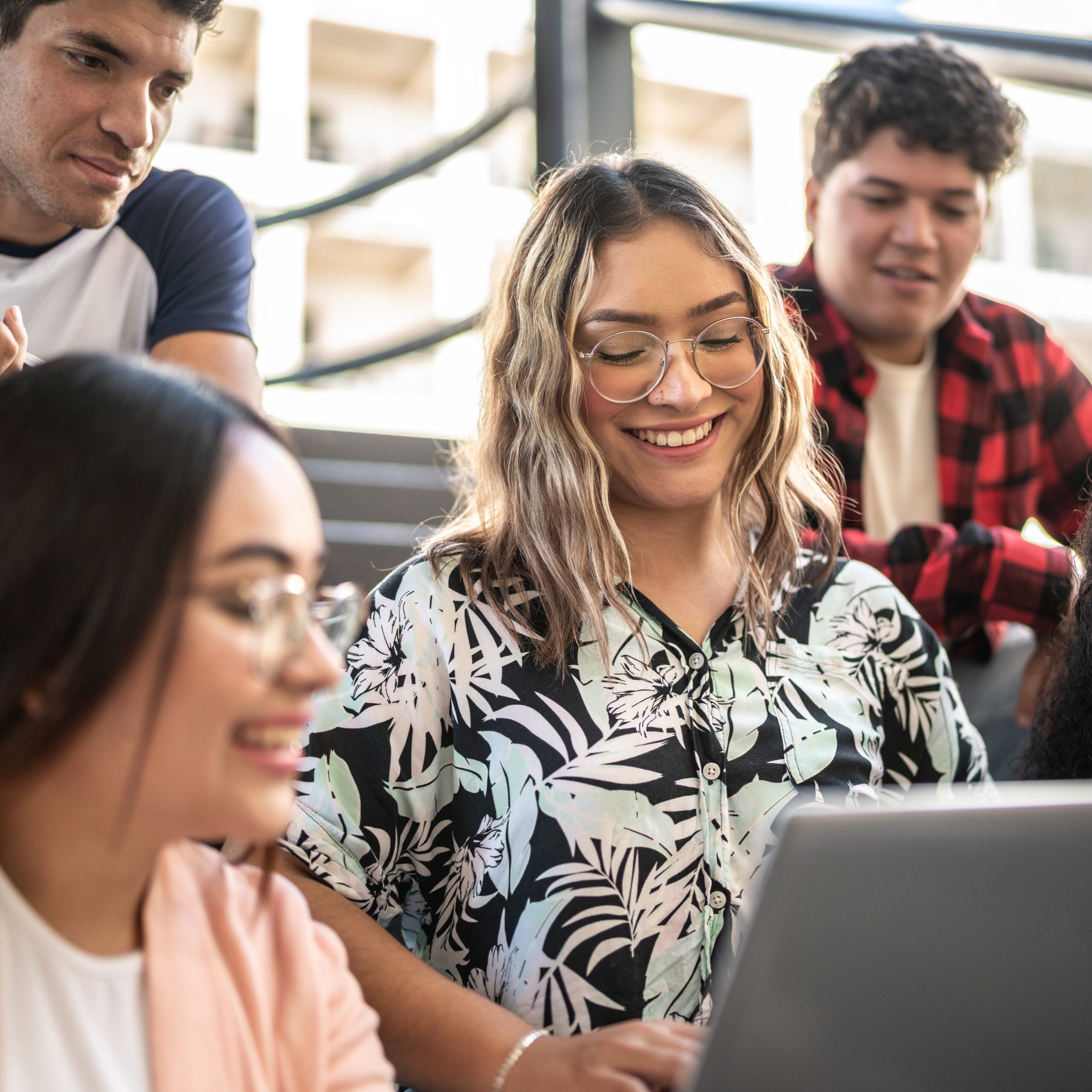 Blonde Frau schaut auf ihren Laptop, umgeben von 3 weiteren Personen.