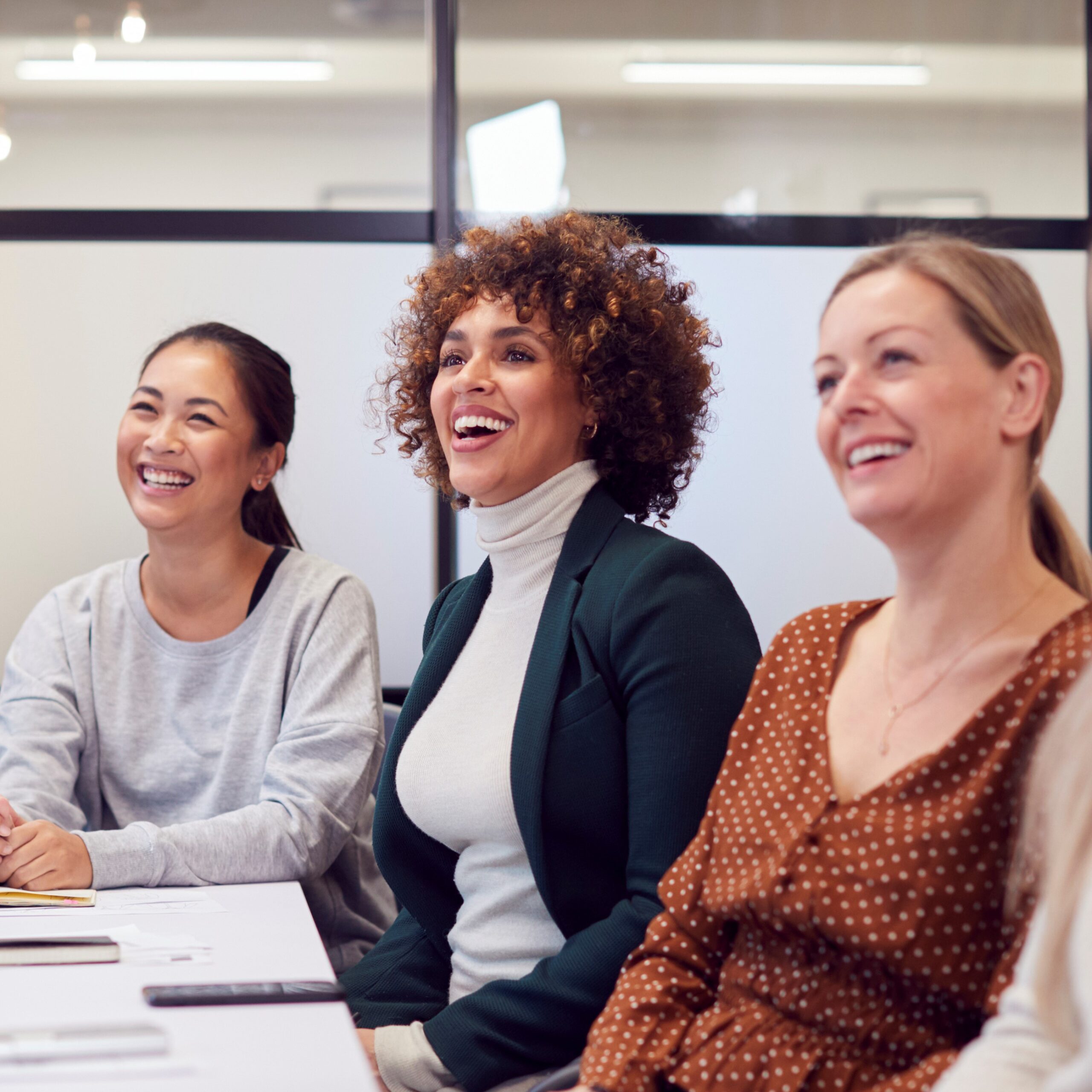 Drei Frauen mit unterschiedlichen Herkünften sitzen in einem Büro und lachen.
