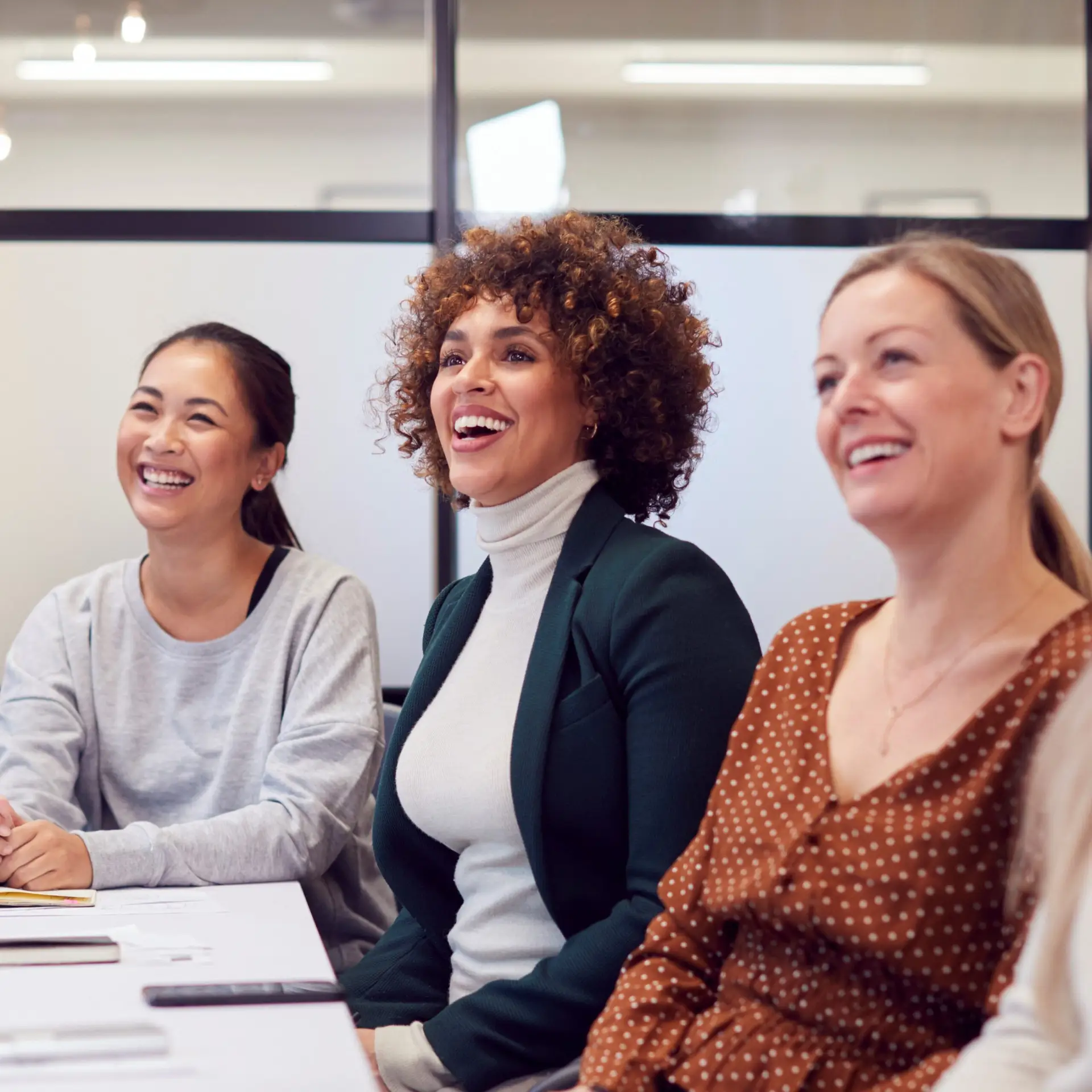 Drei Frauen mit unterschiedlichen Herkünften sitzen in einem Büro und lachen.
