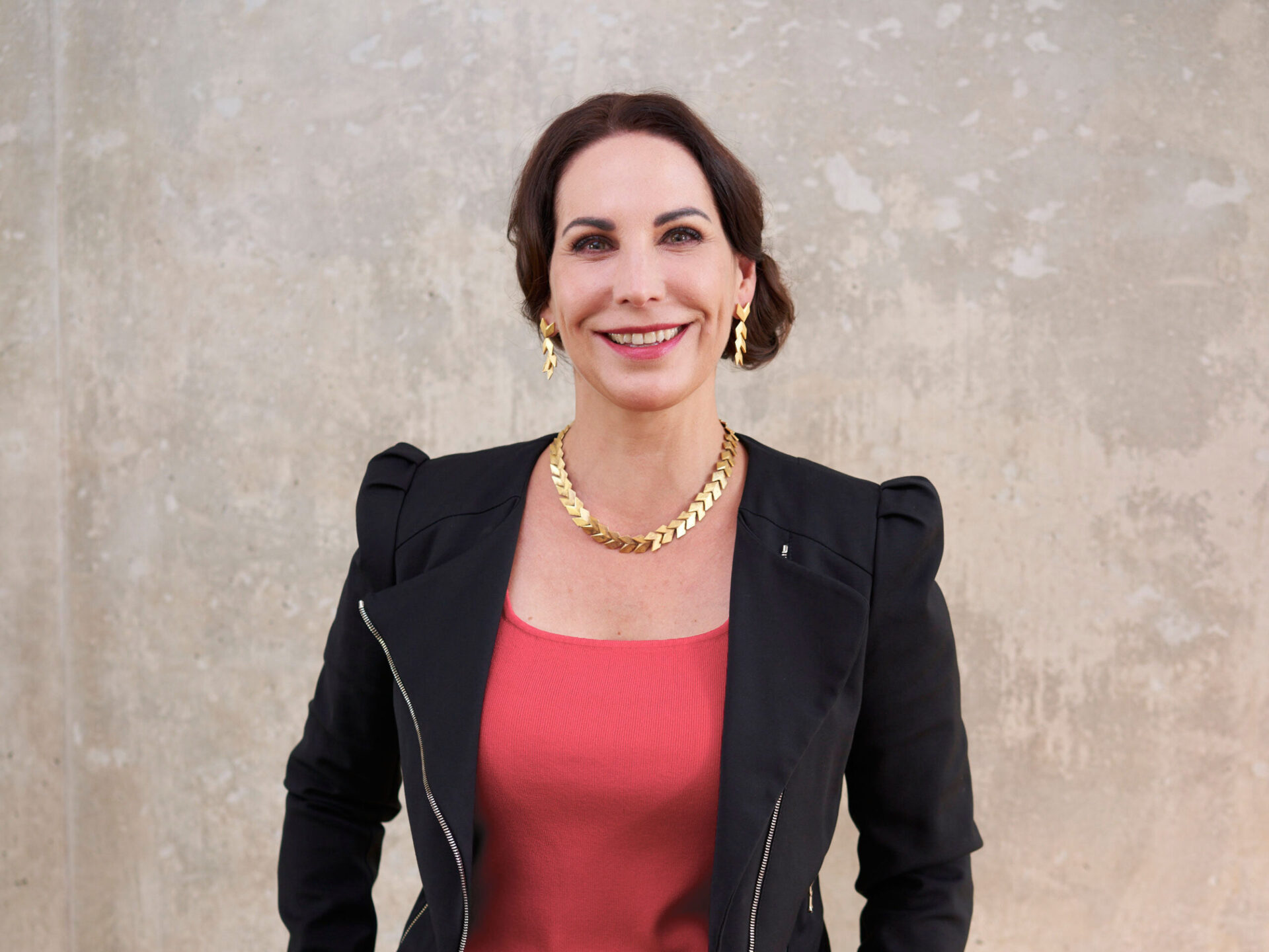 Portrait von Katrin Winkler in einer schwarzen Jacke und mit goldenem Schmuck.