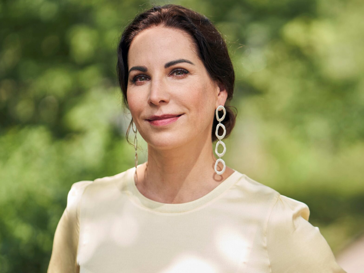Portrait von Prof Dr Katrin Winkler, lange Statement-Ohrringe, helles T-Shirt, natürliches Licht, grüner Hintergrund