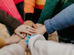 Acht Arme, die ihre Hände aufeinander gelegt haben. Es symbolisiert Teamarbeit und Teamleistung