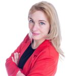 Eine blonde Frau im roten Blazer, Prof. Dr. Sandra Niedermeier, schaut mit verschränkten Armen seitlich über die Schulter lächelnd direkt in die Kamera.