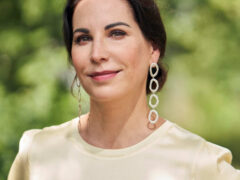 Portrait von Prof Dr Katrin Winkler, lange Statement-Ohrringe, helles T-Shirt, natürliches Licht, grüner Hintergrund