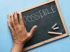 Ein dekoratives Header-Bild für Leading Change Haltung statt Methode, eine Schiefertafel auf der Possible steht, eine Hand verdeckt einen Teil, es suggeriert, ein "im"- also würde eigentlich Impossible stehen.