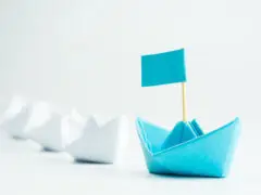 berufsbegleitender MBA für internationale Führungskräfte, eine Reihe von Papierschiffchen, ein blaues Papierschiffchen mit einem Fähnchen an ihrer Spitze. Das "Leader-Ship"