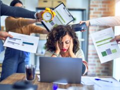 Stress im Job: überforderte Mitarbeiterin am Laptop im Büro mit vielen gleichzeitigen Anforderungen