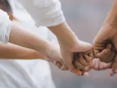 Das Bild zeigt eine nah herangeholte Aufnahme im Panoramaformat, die Zusammenhalt und Vernetzung veranschaulicht. Im Mittelpunkt stehen die Hände mehrerer Personen, die im Kreis stehen und ihre Fäuste in der Mitte zusammenführen (Fist Bump). Die Kleidung der Beteiligten ist in neutralen, hellen Tönen gehalten, während der Hintergrund unscharf bleibt. Das Motiv steht sinnbildlich für Teambuilding, Zusammenhalt, Vertrauen, gegenseitige Unterstützung und gelungene Zusammenarbeit.